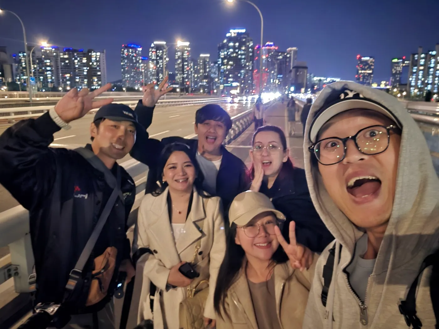 The team out on a bridge at night, the lit Seoul skyline behind them