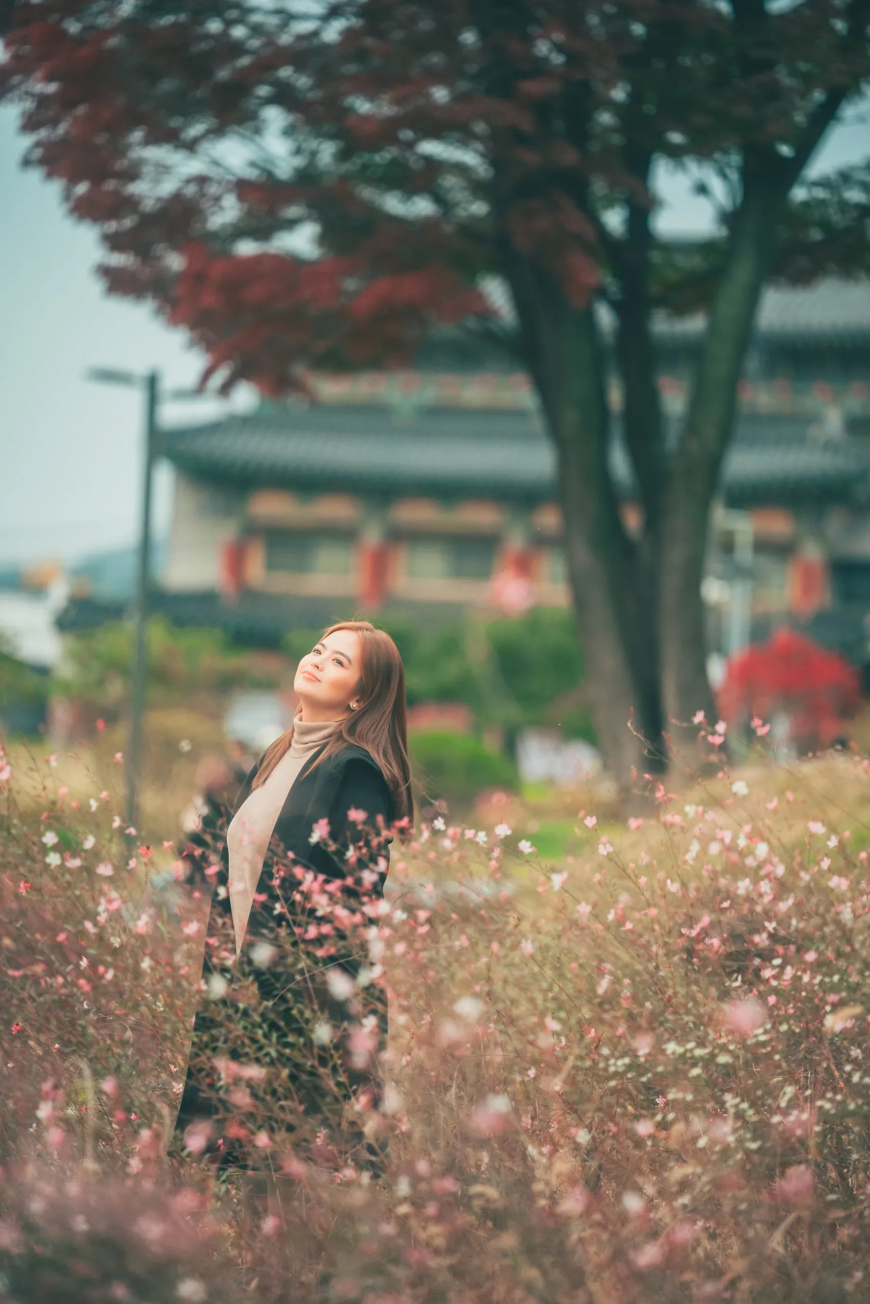 Bea Binene among pink flowers by a hanok wall