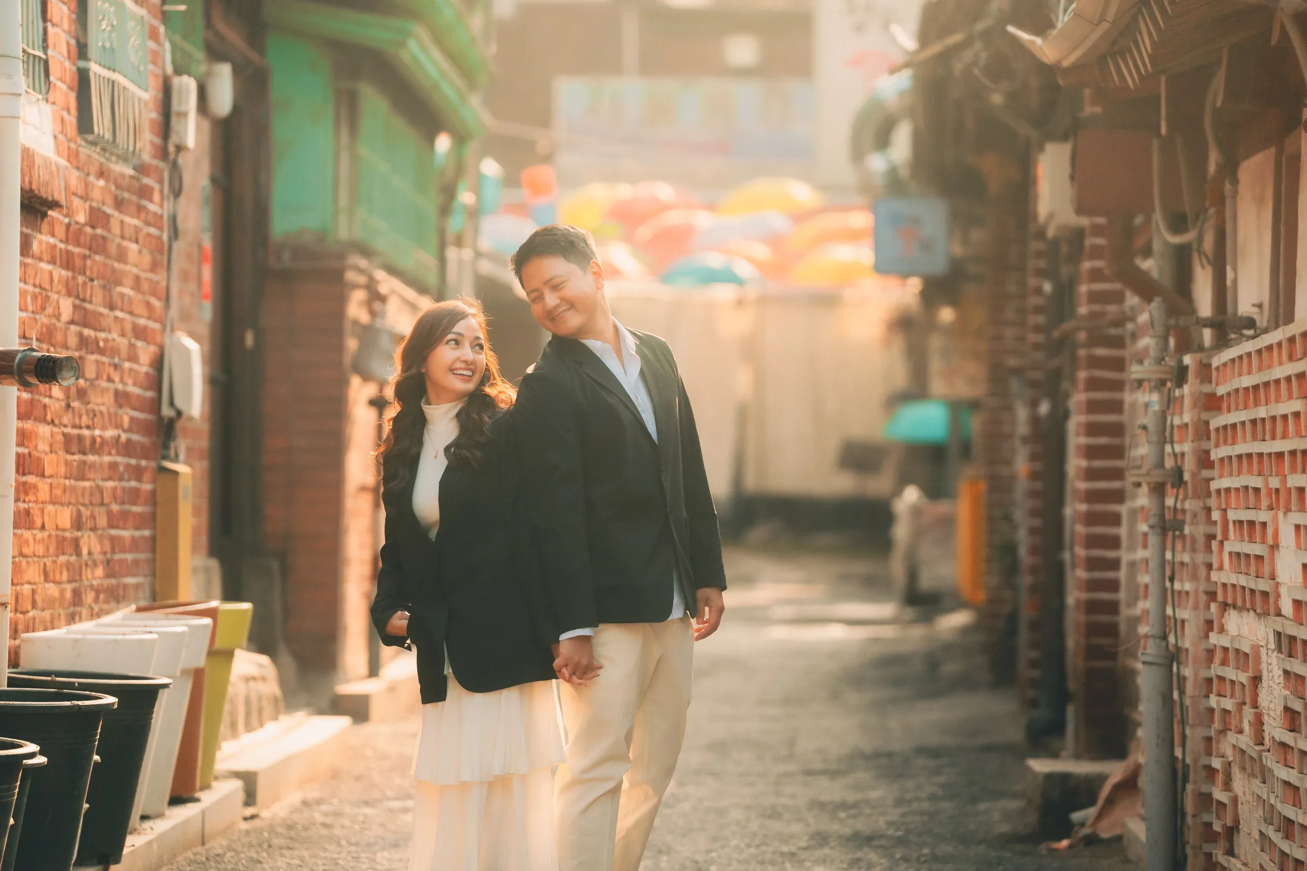 Walking a brick alley with colorful umbrellas strung overhead.