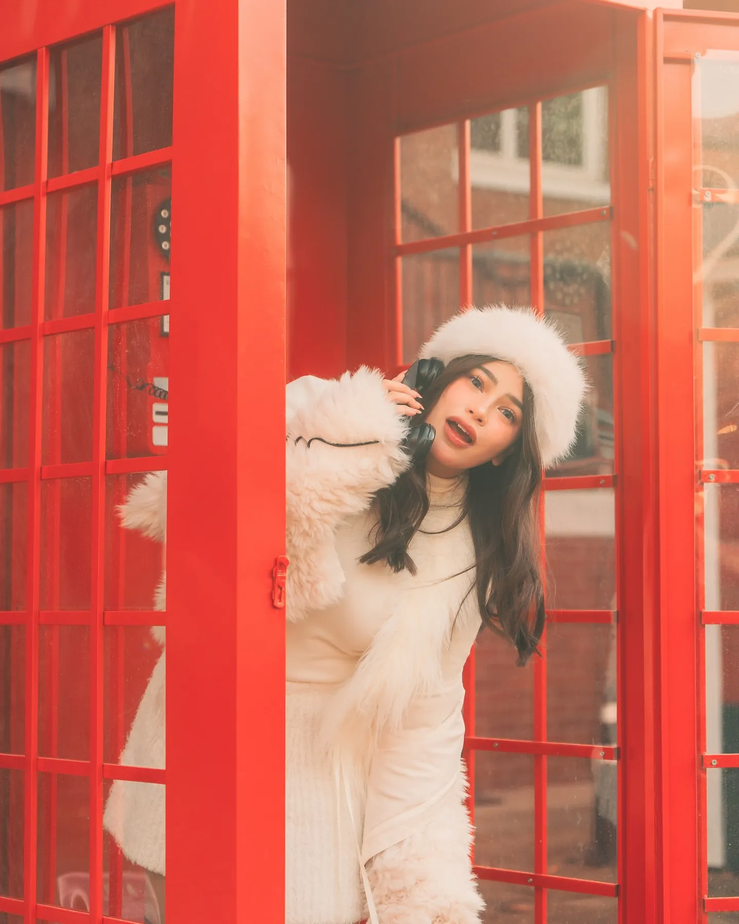 Denise Laurel leaning out of a red telephone booth with the receiver