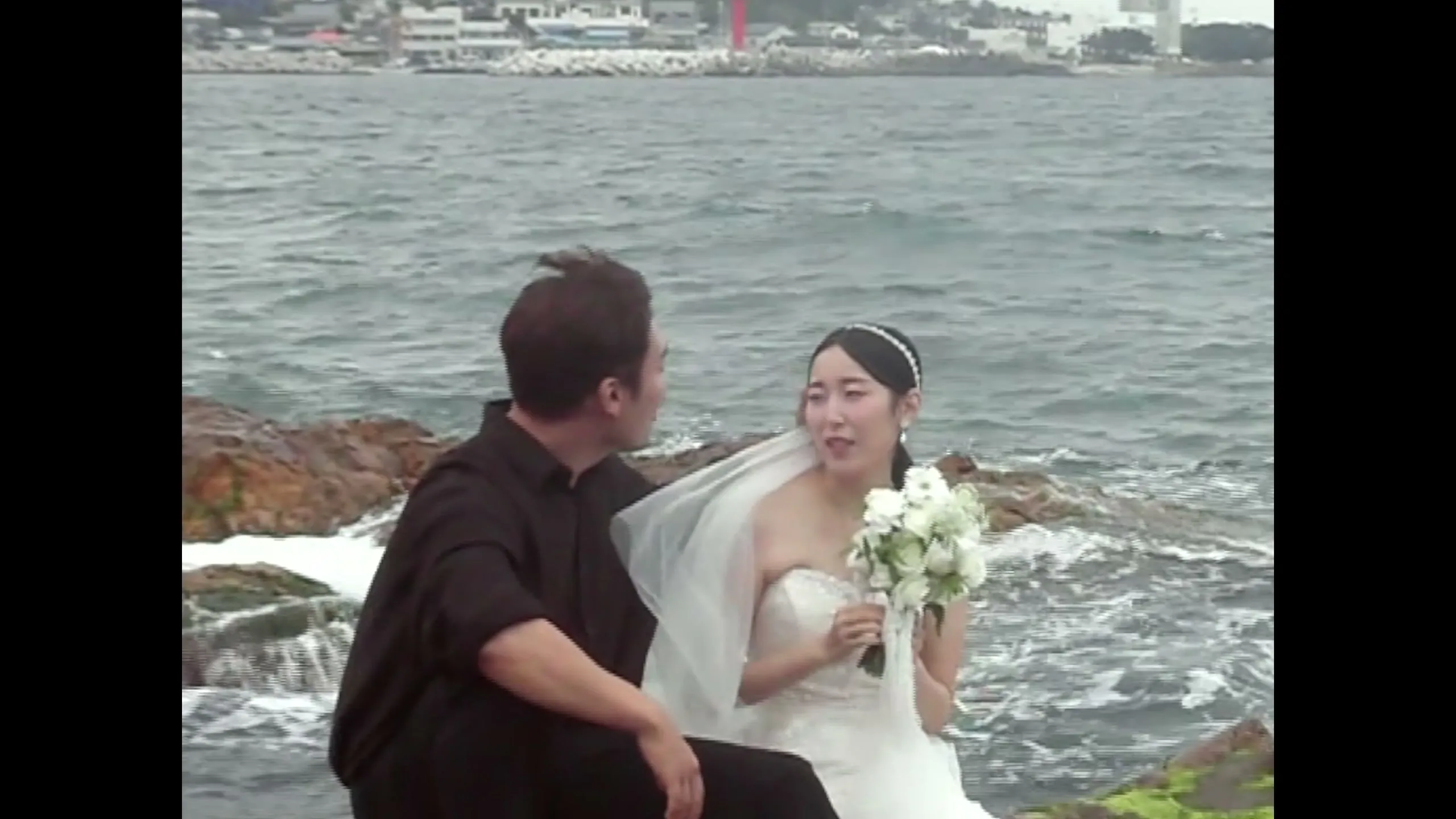 The couple standing together on the mossy tide rocks, the sea coming in behind them.
