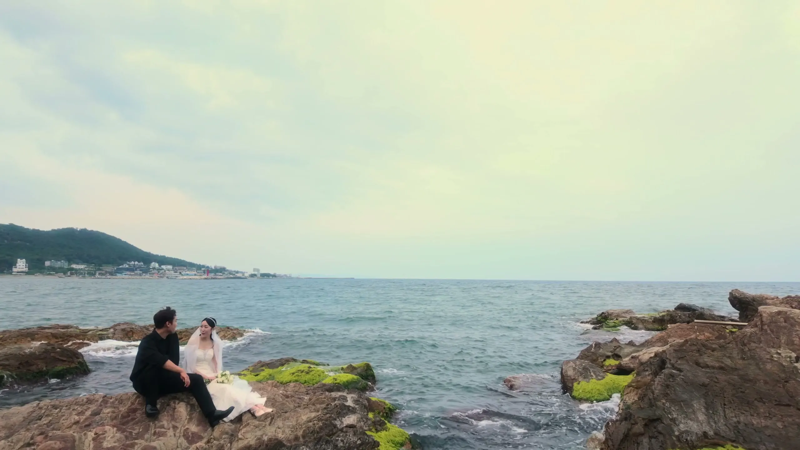 The two of them small on the rocks by the sea, seated close together as the waves break below.