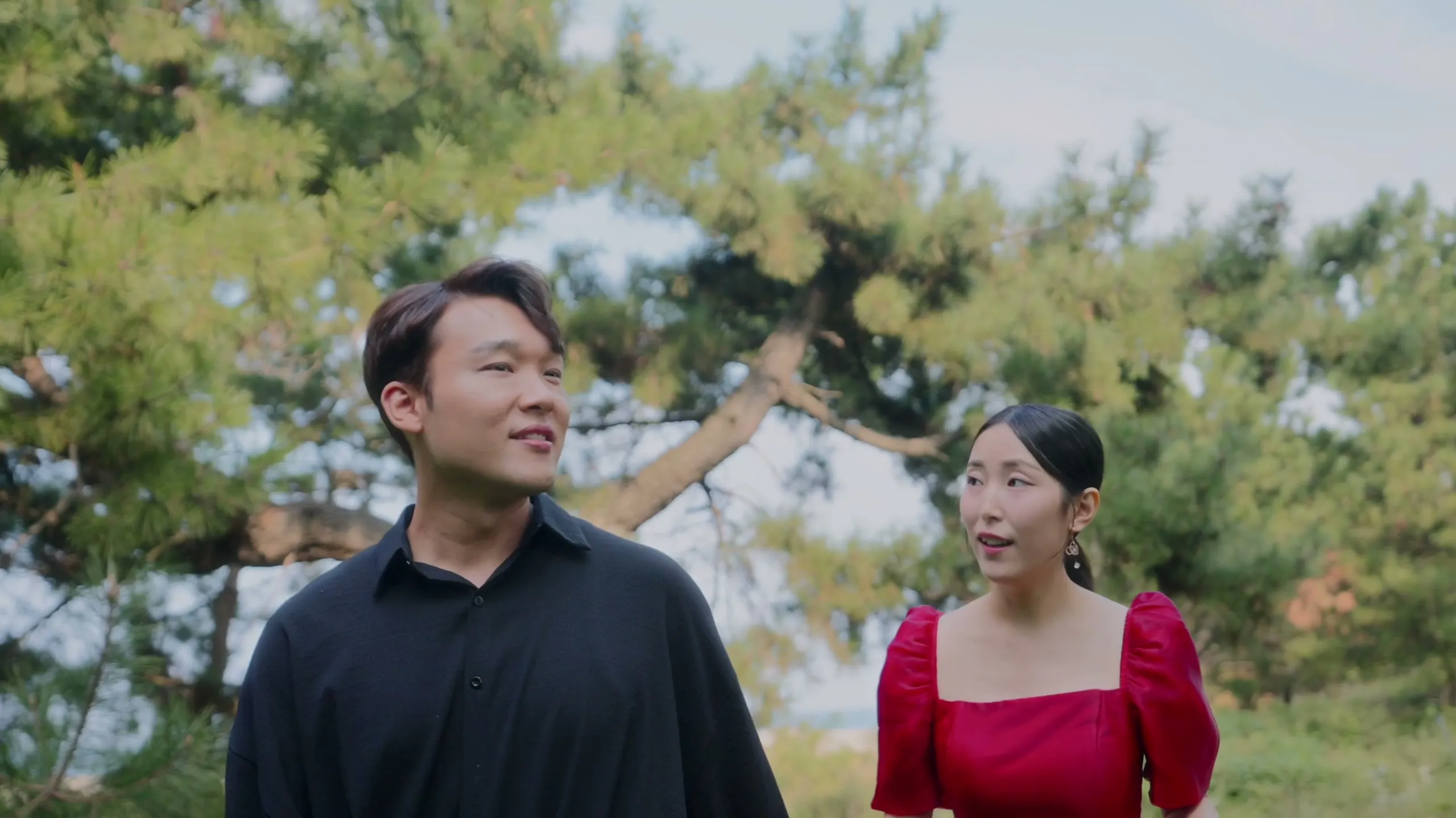 In the garden, the bride in a red dress and the groom in black, close together and smiling.