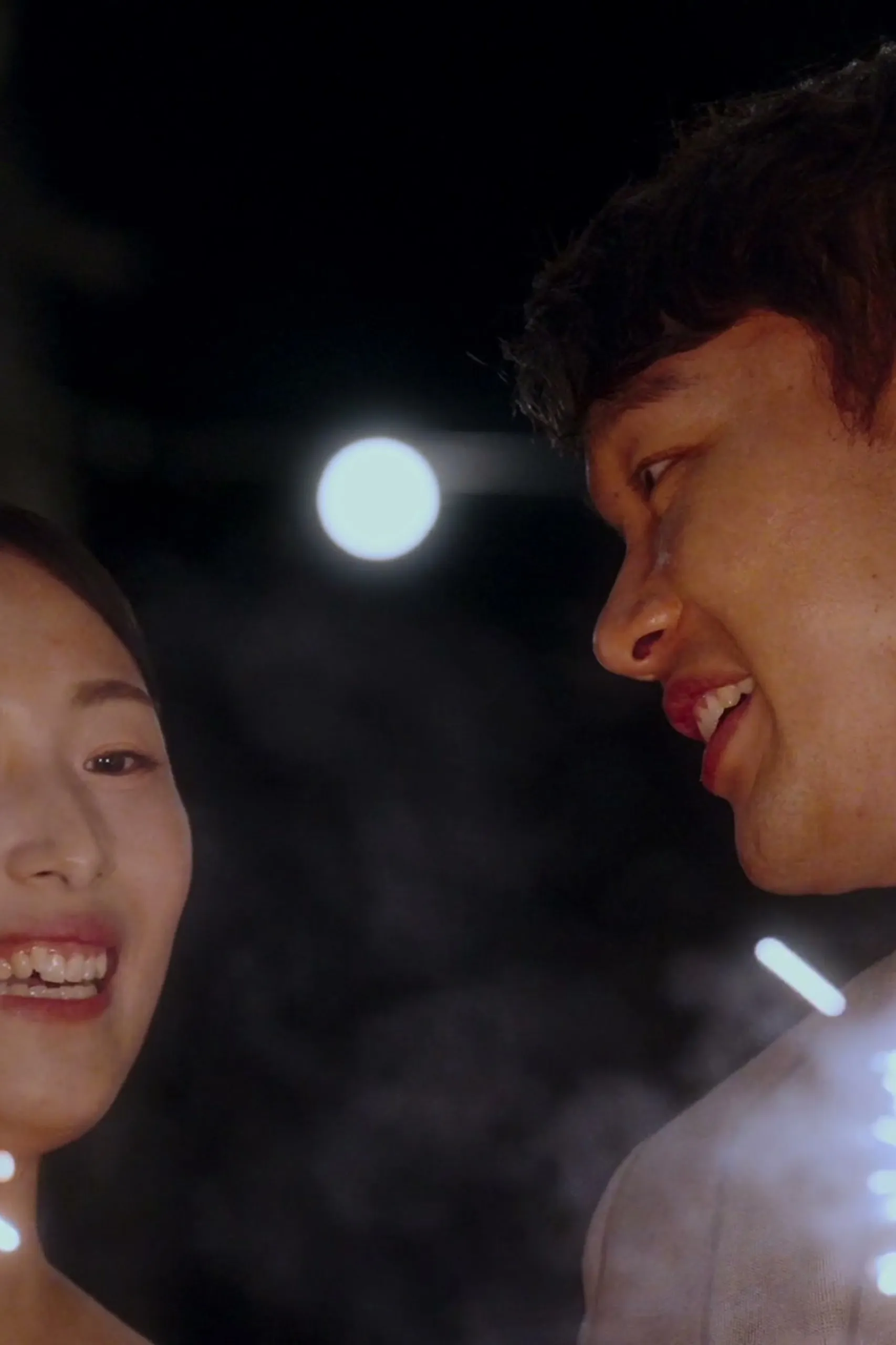 At night, their foreheads close over a lit sparkler, both faces glowing in the dark.