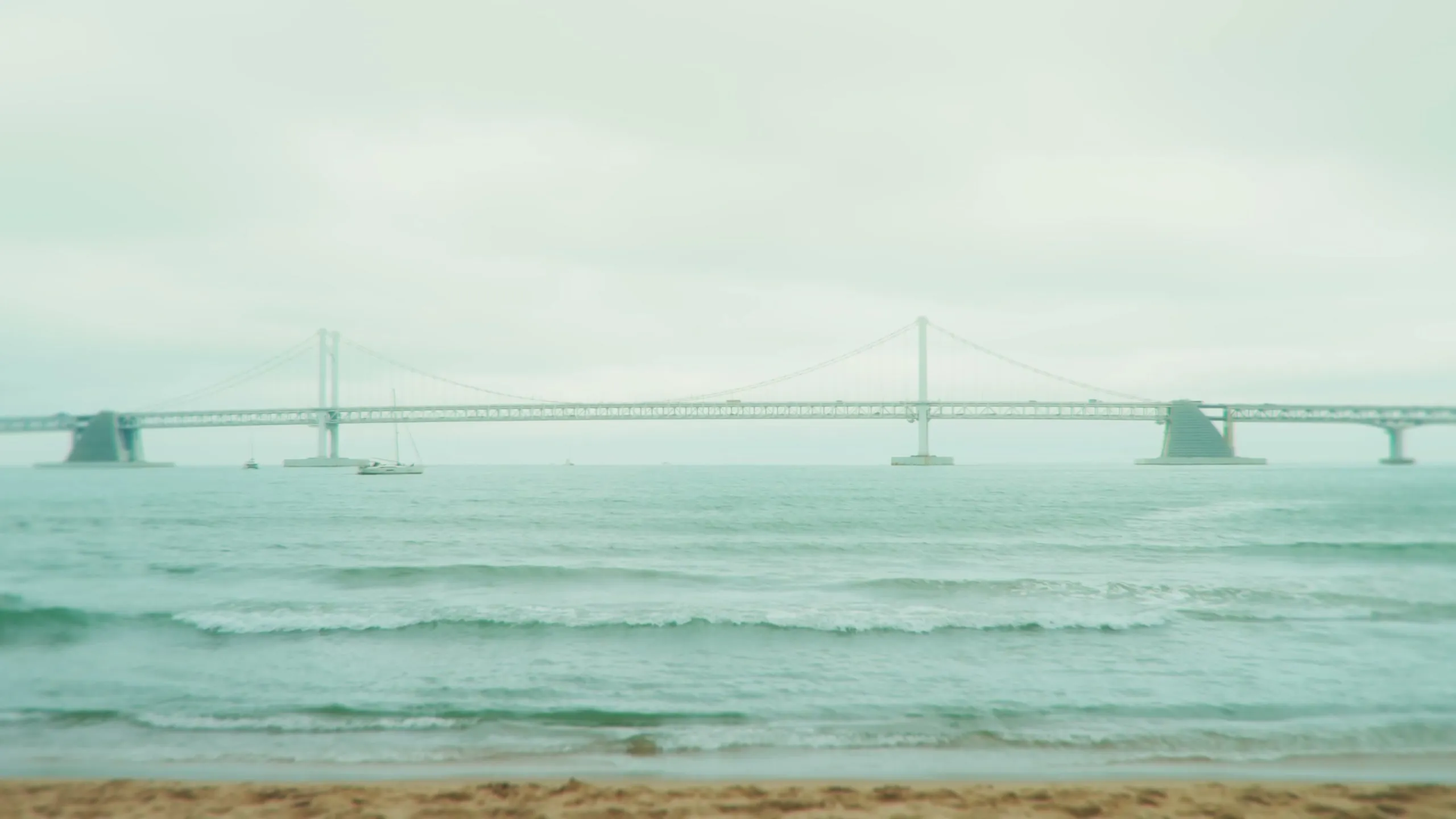 Gwangan Bridge across a pale mint sea under a grey overcast sky.