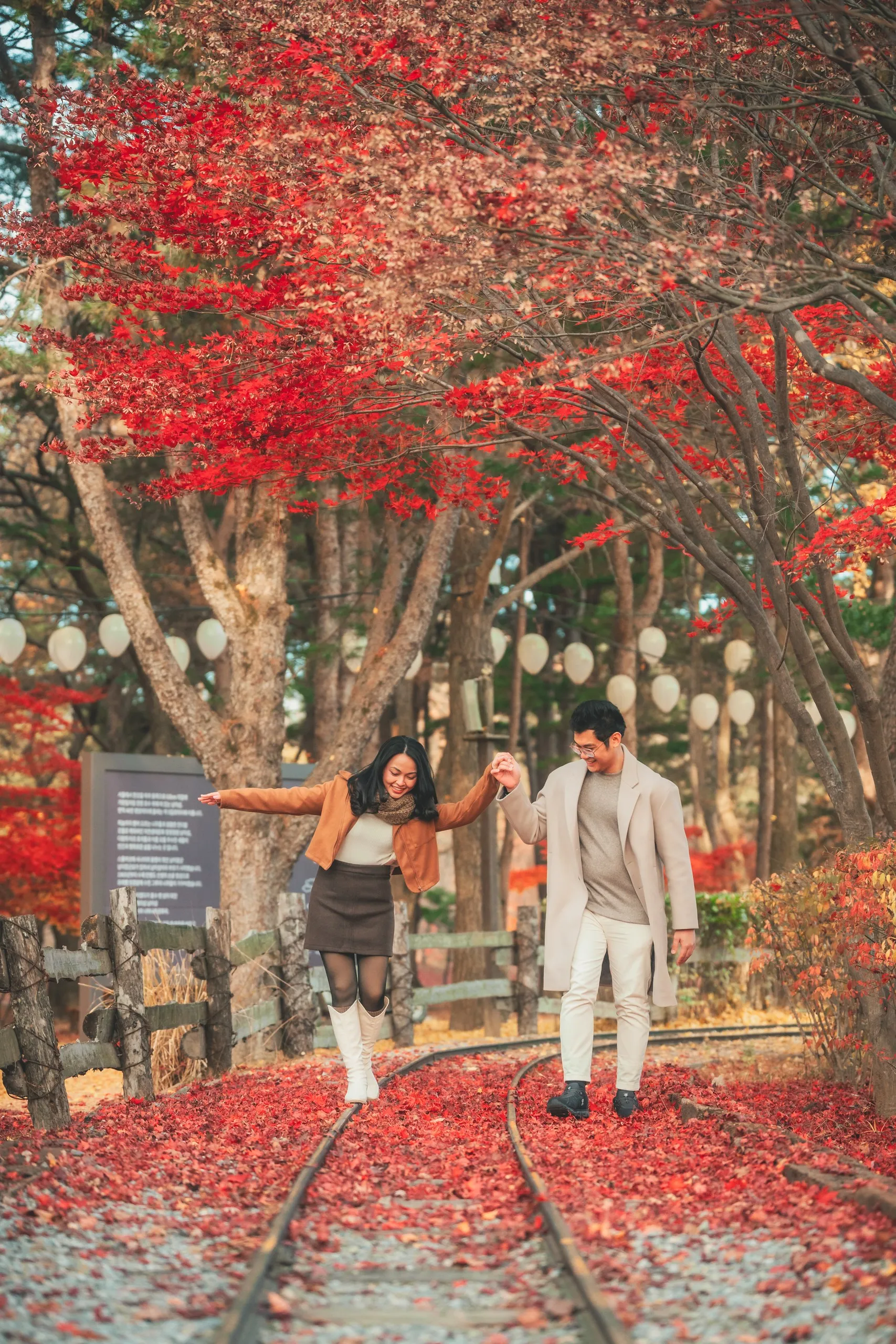 A couple holding hands on rail tracks under red maples