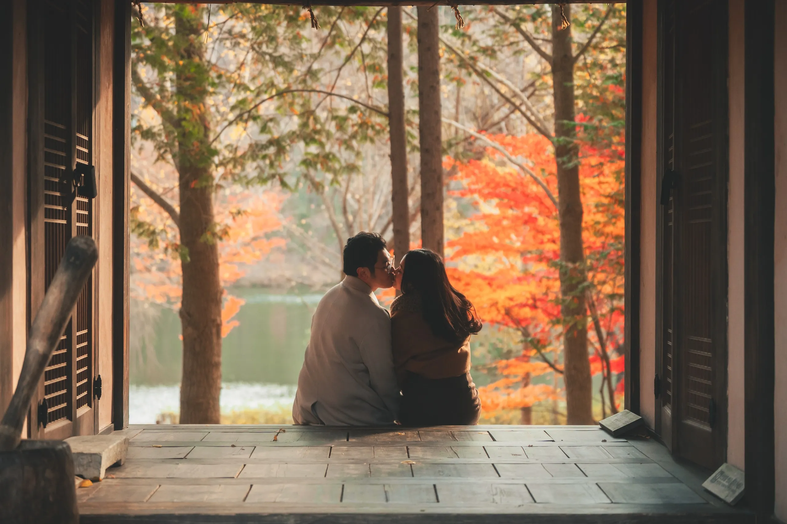 A couple sitting in a pavilion doorway over an autumn lake