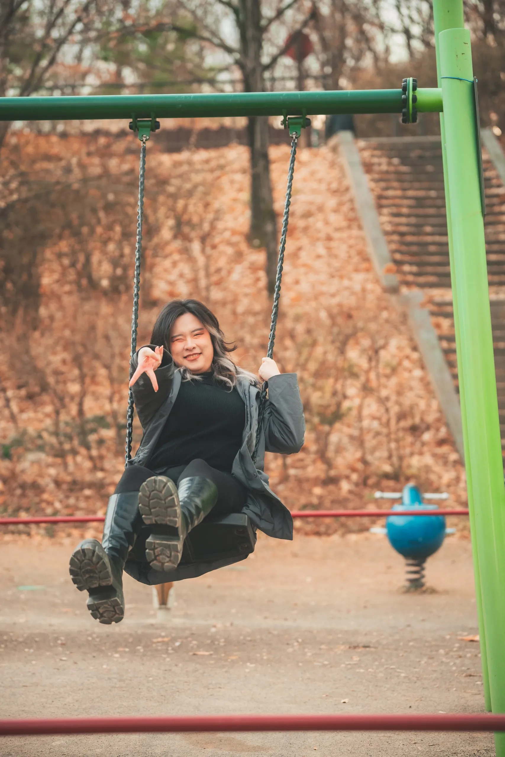 Tracy mid-swing on the green playground swing.