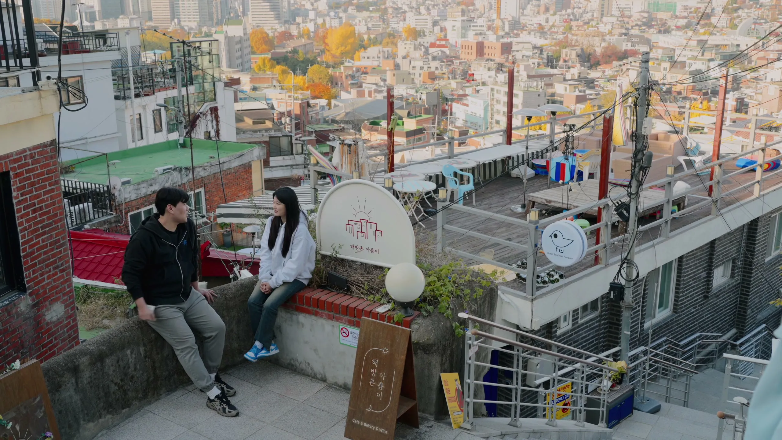 The two sitting on a rooftop ledge above the tiled roofs of Haebangchon.